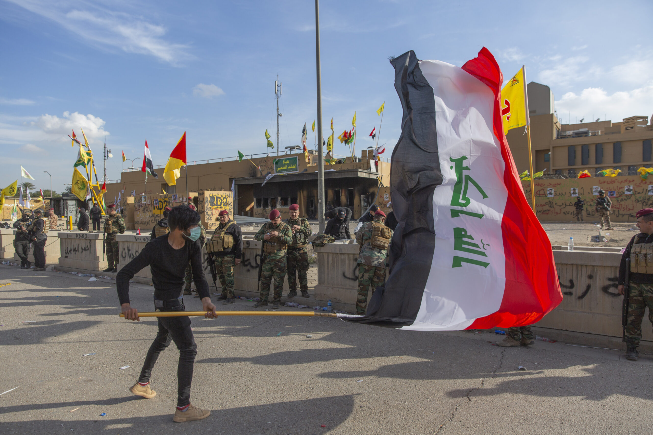 A man waves the Iraqi flag while Iraqi soldiers are deployed in front of the U.S. Embassy in Baghdad, Iraq, Jan. 1. AP Photo/Nasser Nasser)