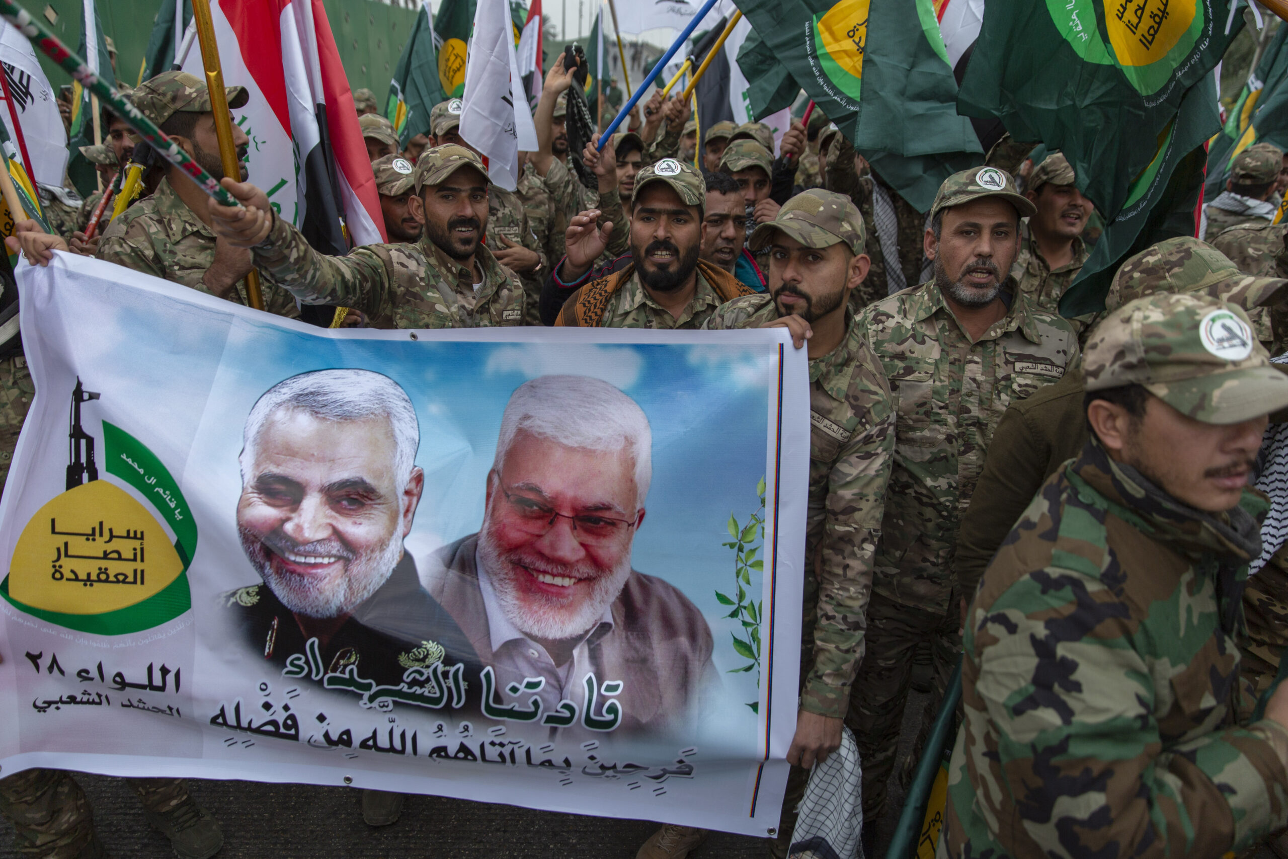 Iraqi militiamen march while carrying a picture of Qassim Suleimani, Iran's Quds Force commander, left, and Abu Mahdi al-Muhandis, deputy commander of Iran-backed militias in Iraq known as the Popular Mobilization Forces, with Arabic that reads "our Martyr leaders," in Baghdad, Iraq, Jan. 4. (AP Photo/Nasser Nasser)