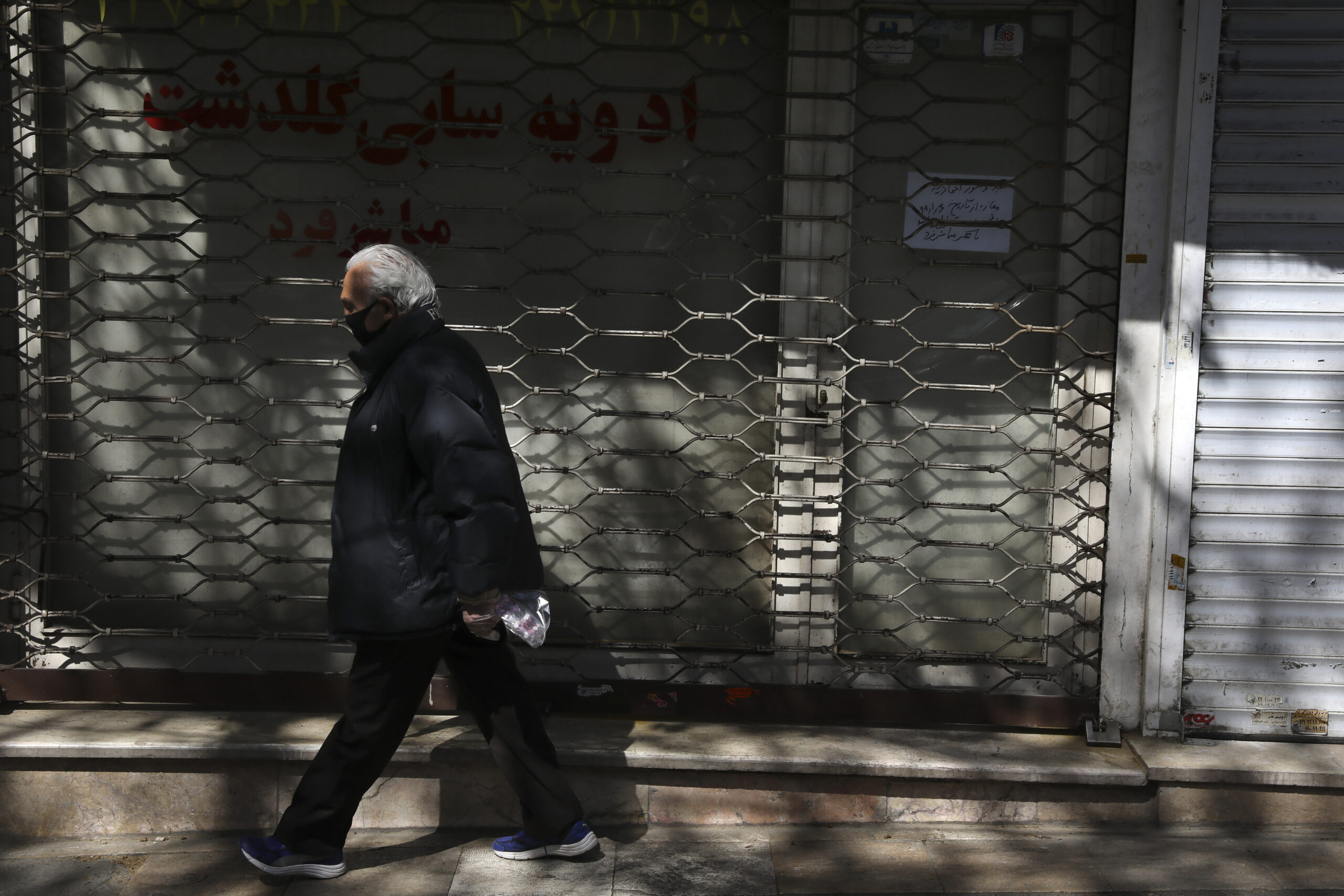 A man wearing a face mask and gloves to protect against the novel coronavirus walks past closed shops in northern Tehran, Iran, April 4. (AP Photo/Vahid Salemi)