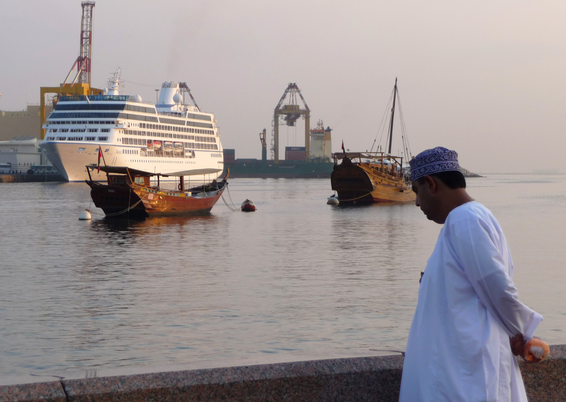 An Omani man views the M/S Nautica, left, as it sails near traditional Omani boats and prepares for a port stop in Muscat, Oman. (AP Photo/ Sebastian Abbot)