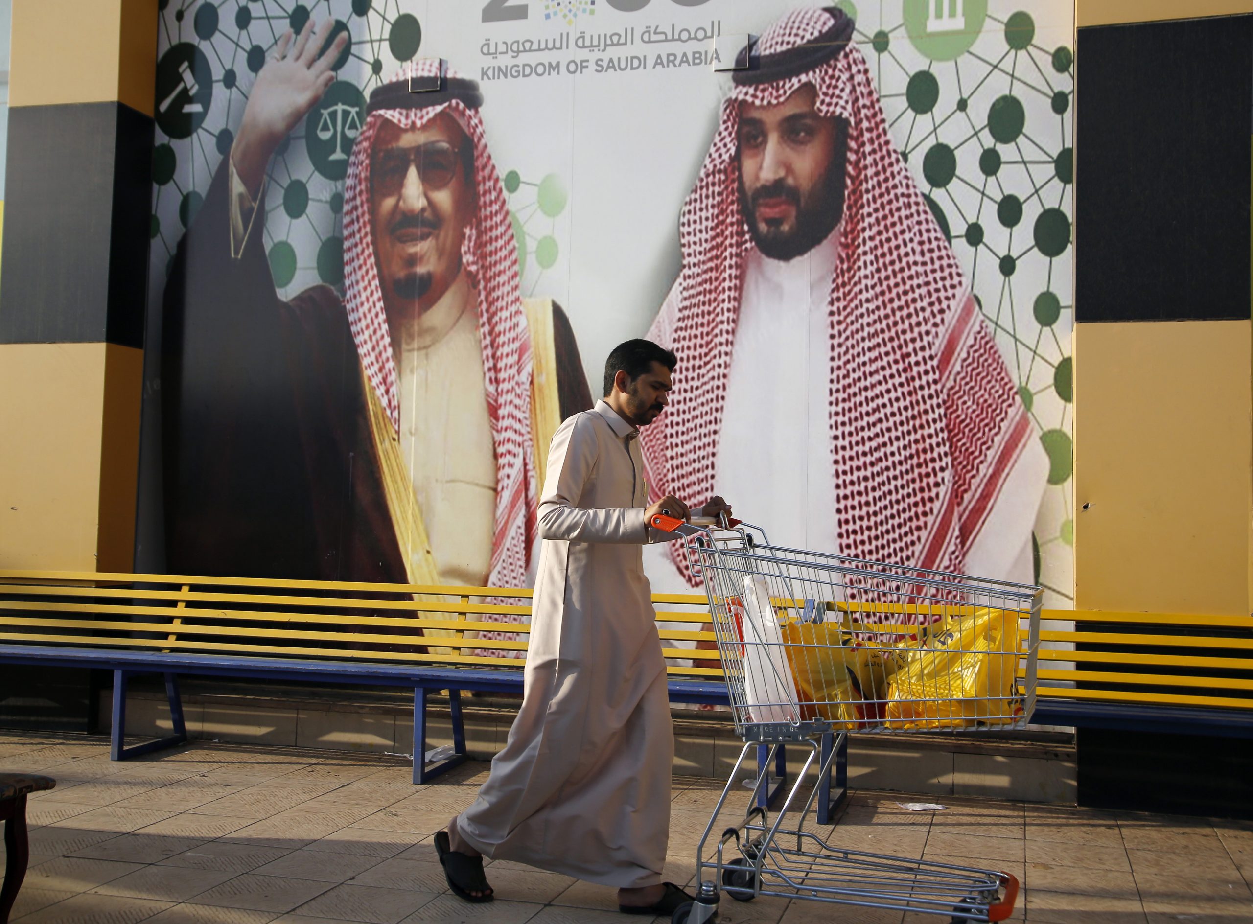 People walk past a banner showing Saudi King Salman bin Abdulaziz, left, and Crown Prince Mohammed bin Salman, outside a mall in Jeddah, Saudi Arabia, Dec. 6, 2019. (AP Photo/Amr Nabil)