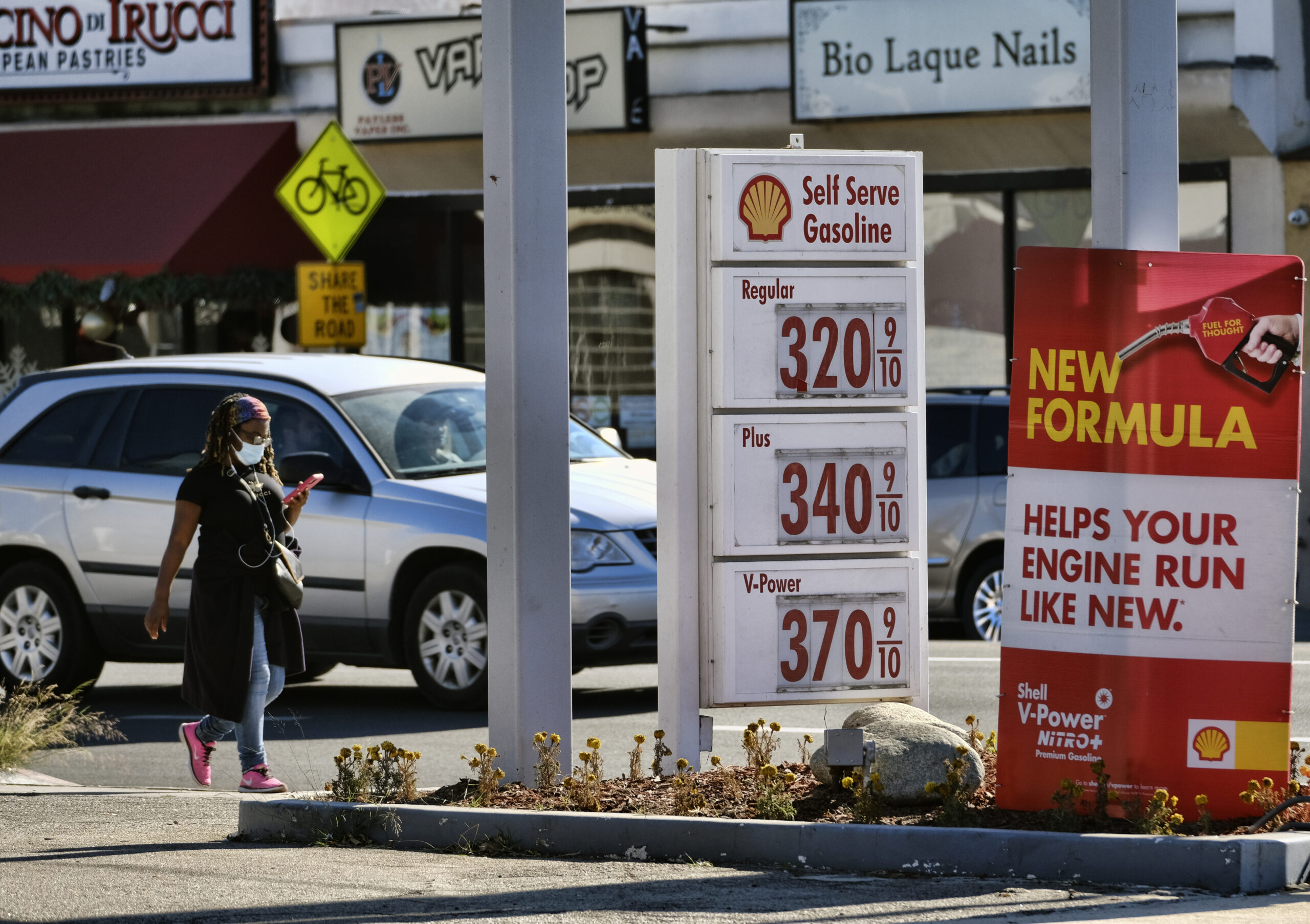 A masked pedestrian walks past a self-service gas station in Los Angeles, California, Dec. 6, 2020. (AP Photo/Richard Vogel)