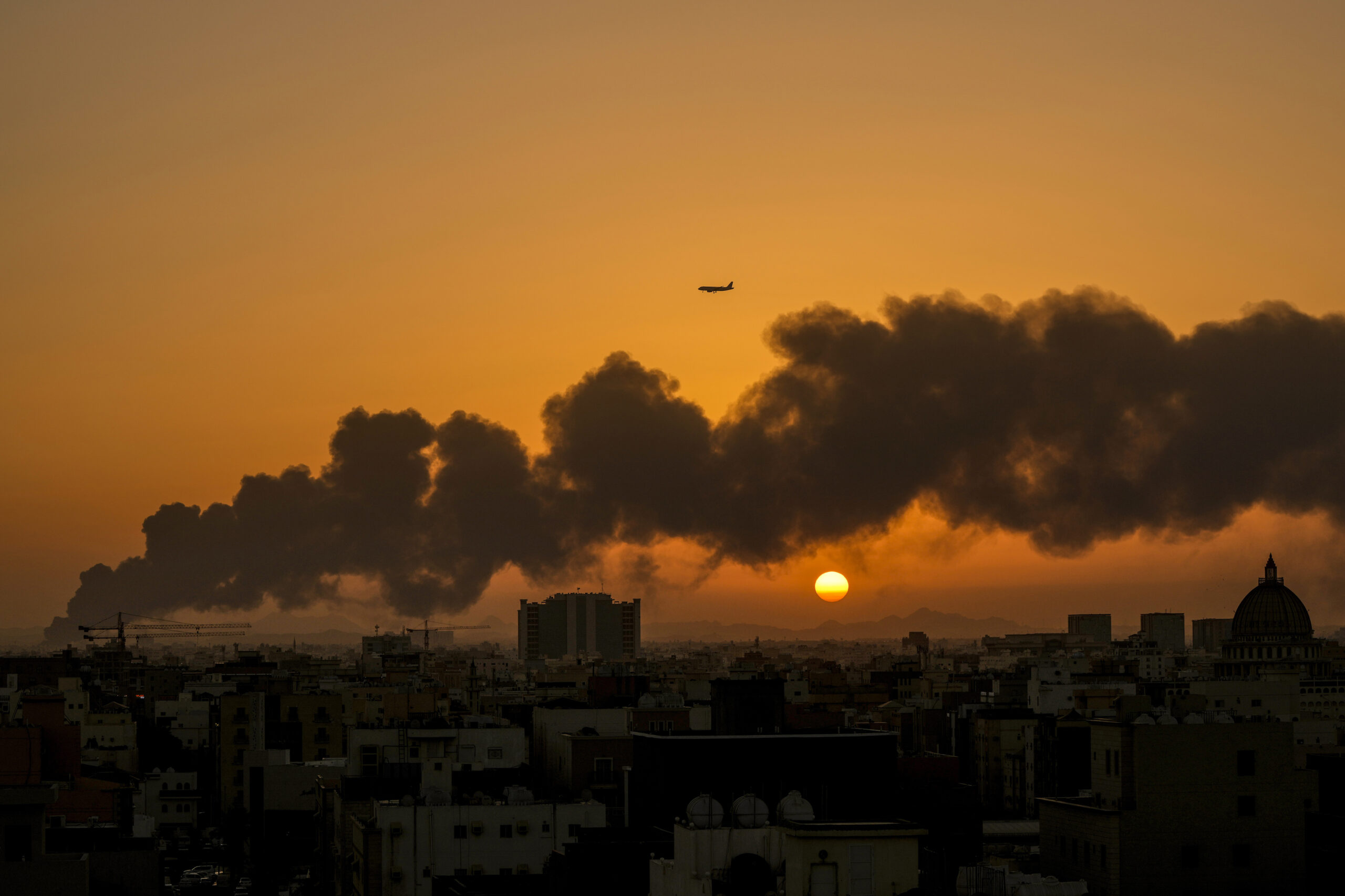 A passenger airplane flies over a smoldering fire at a Saudi Aramco oil depot after a Houthi-claimed attack in Jeddah, Saudi Arabia, March 26. (AP Photo/Hassan Ammar)
