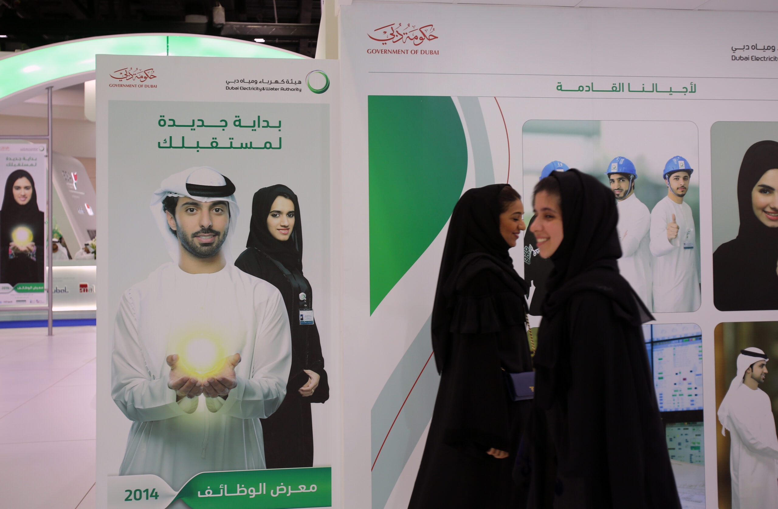 Emirati women pass by posters at a government stand during the Careers UAE opening exhibition for UAE citizens in Dubai, United Arab Emirates, April 22, 2014. (AP Photo/Kamran Jebreili)