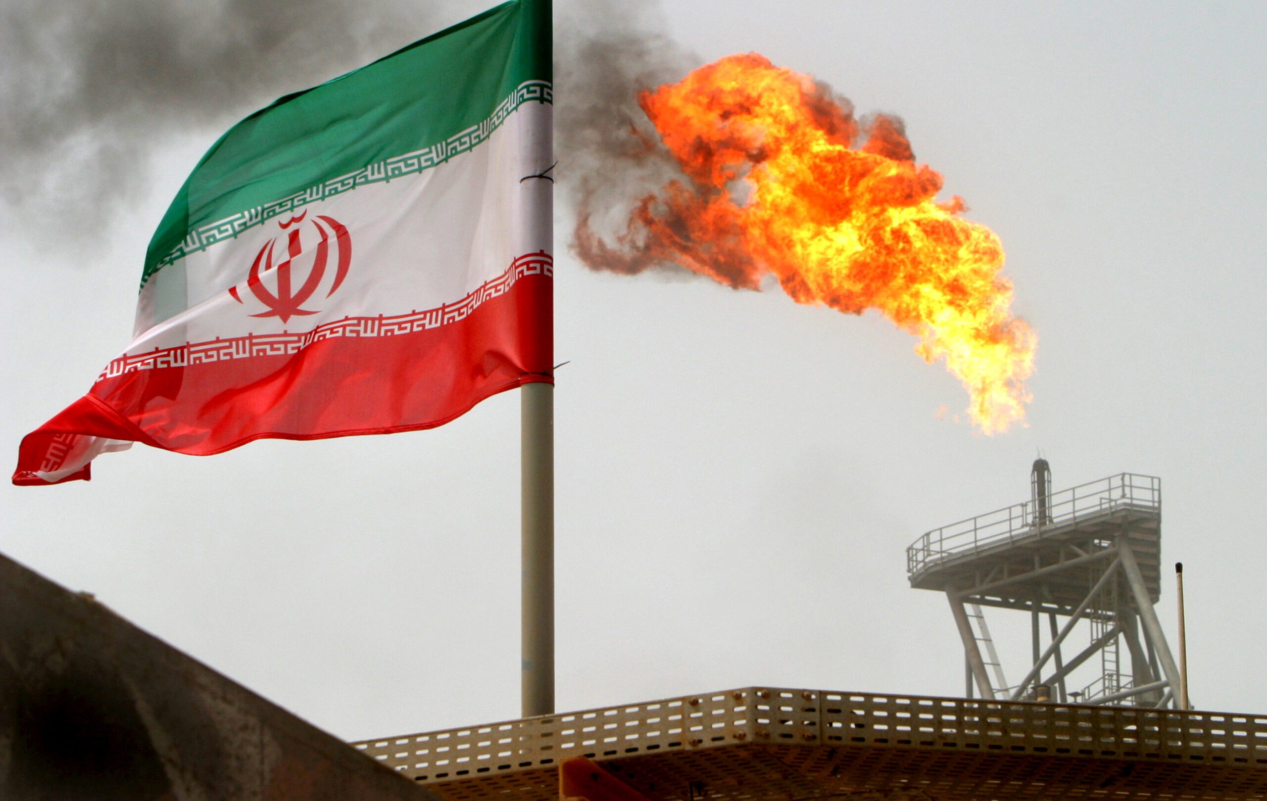 A gas flare on an oil production platform is seen alongside an Iranian flag in the Gulf, July 25, 2005. (REUTERS/Raheb Homavandi)