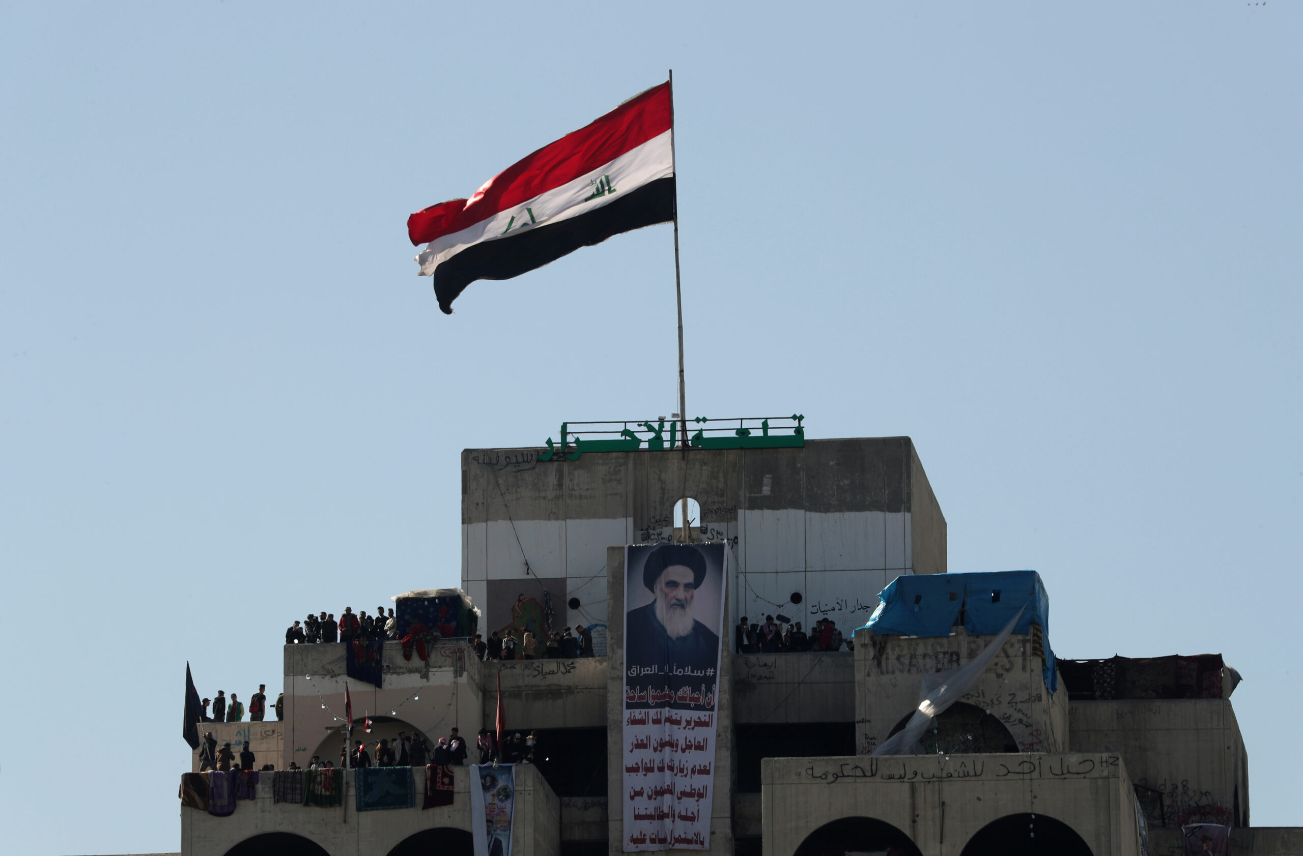 A poster of Iraqi Shia cleric, Grand Ayatollah Ali al-Sistani, is seen as Iraqi demonstrators stand on a high-rise building during ongoing anti-government protests in Baghdad, Iraq, January 26, 2020. (REUTERS/Thaier al-Sudani)