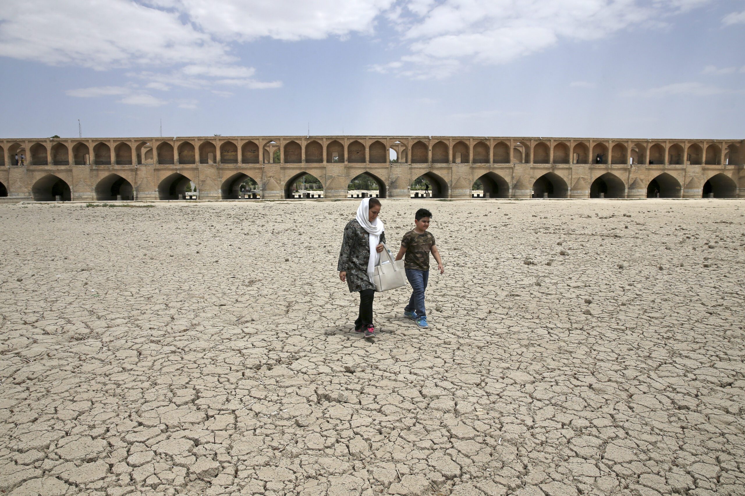 A woman and a boy walk on the dried up riverbed of the Zayanderud river that no longer runs under the Si-o-Seh-Pol bridge in Isfahan, Iran, July 10, 2018. (AP Photo/Vahid Salemi)