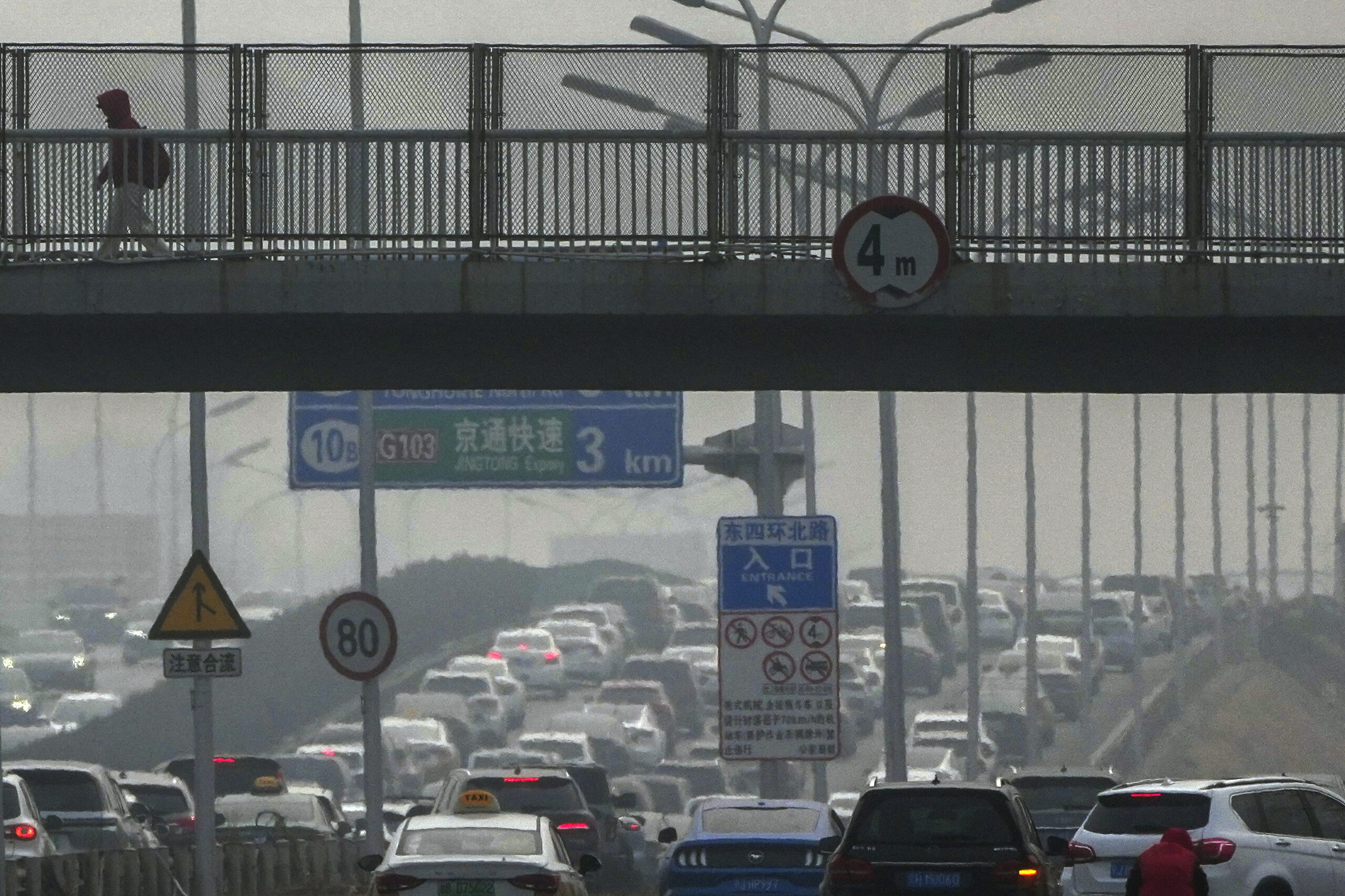 A resident walks across a pedestrian overhead bridge as motorists drive on a city highway clogged with heavy traffic in Beijing, March 1. (AP Photo/Andy Wong)