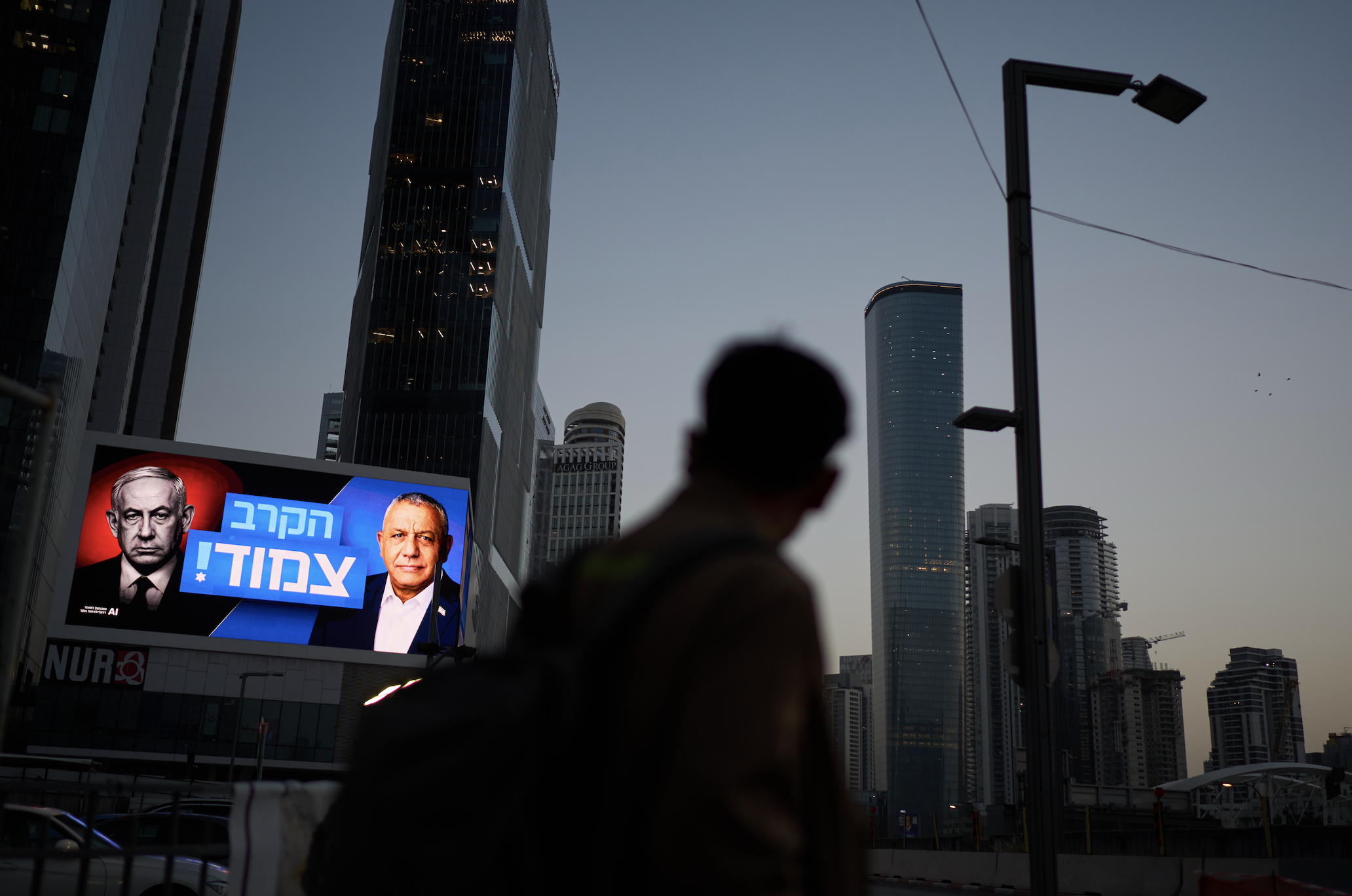 A pedestrian passes a campaign billboard featuring Israeli Prime Minister Benjamin Netanyahu, left, and his main rival, opposition candidate Gadi Eisenkot, with a message in Hebrew that reads "The race is tight," October 23, in Tel Aviv, Israel. (AP Photo/David Goldman)